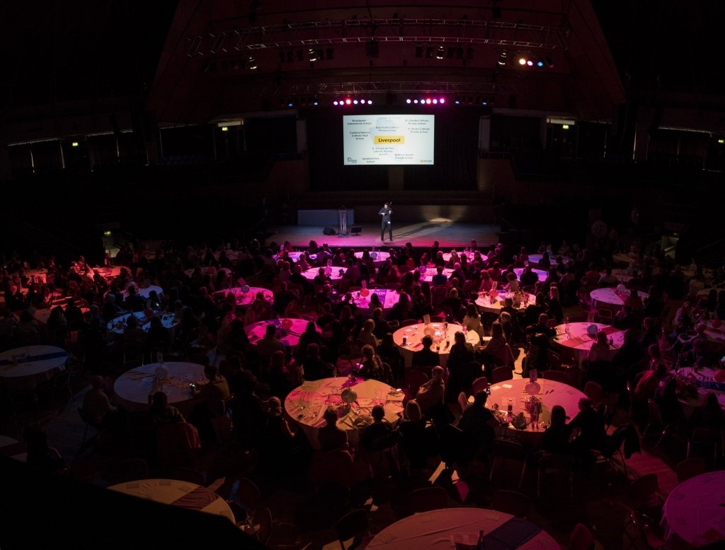 Multiple tables at an awards ceremony in front of a large digital screen